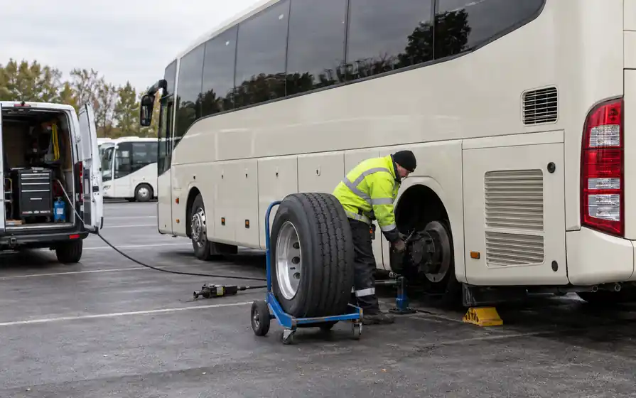 Mobile technician fitting a rear tyre on a cream touring coach.